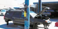 Black SUV with no wheels and hood open in auto body shop bay