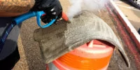 Person steam cleaning a carpeted car floor mat