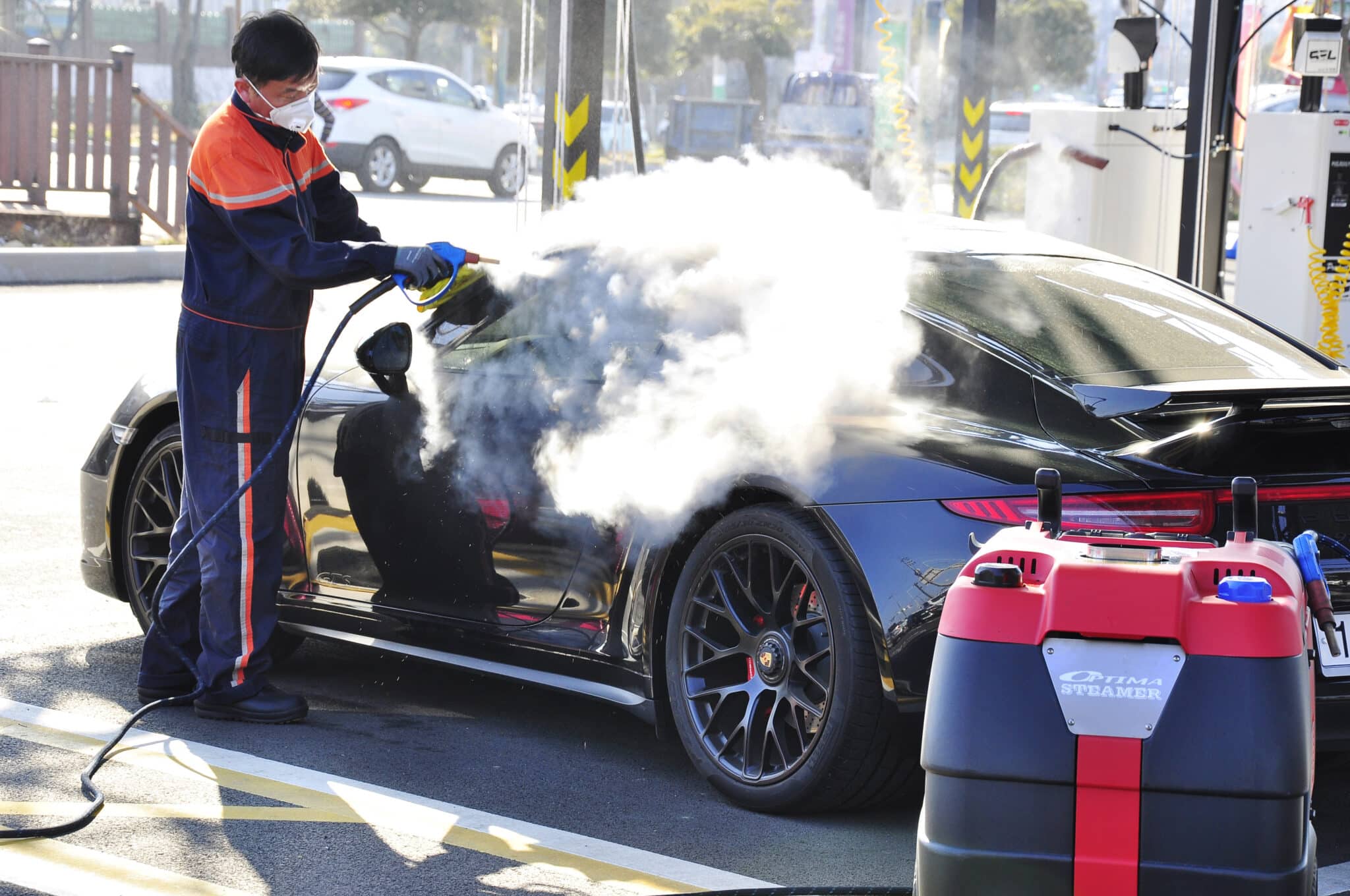 Mobile car wash operator steam cleaning the exterior of a black sports car using the Optima XD Steamer