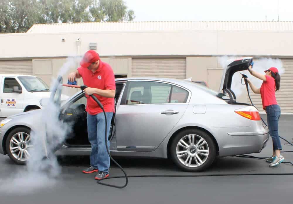 Two mobile car wash operators cleaning a car interior and exterior with the Optima Steamer